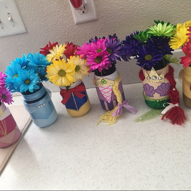 there are many colorful flowers in the jars on the counter top, and one is decorated like a mermaid