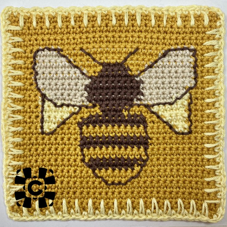 a close up of a knitted square with a bee on it's side