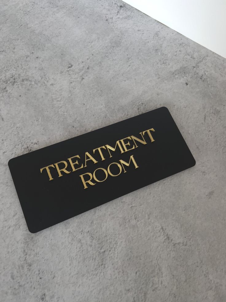 a black and gold sign that says treatment room on the floor in front of a white wall