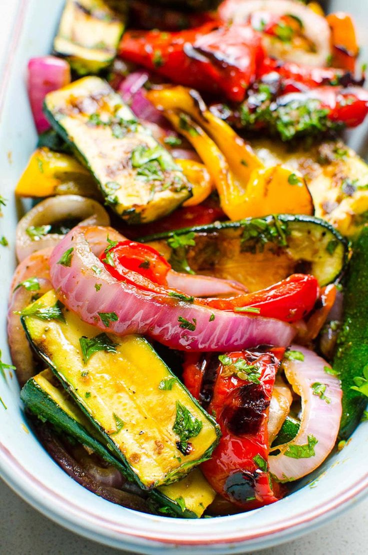 a bowl filled with grilled vegetables on top of a white countertop next to a fork