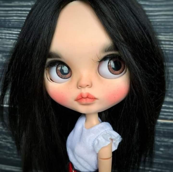 a doll with long black hair wearing a white shirt and red skirt is standing in front of a wooden wall