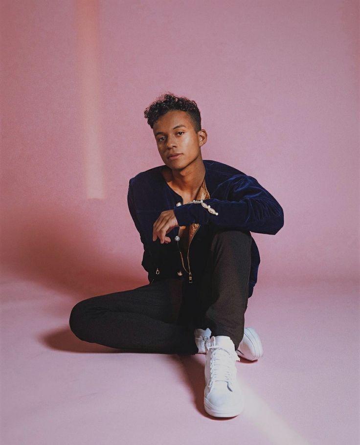 a man sitting on the ground in front of a pink background