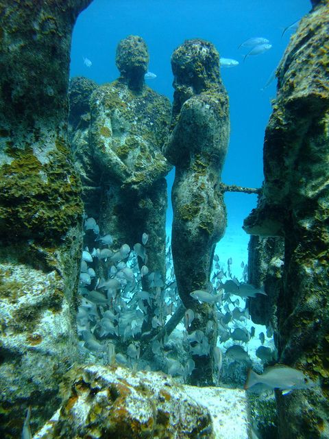 two statues in the water surrounded by corals