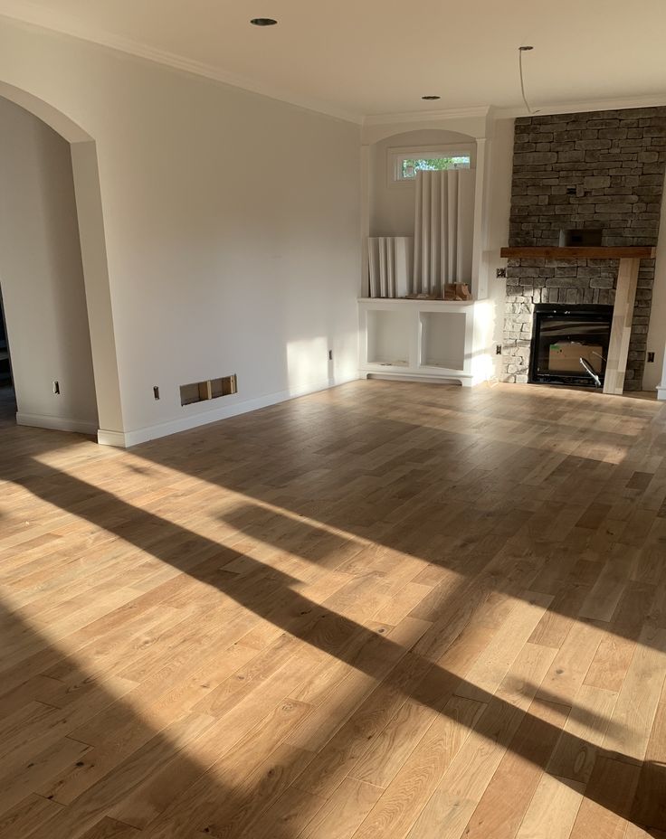 an empty living room with hard wood floors and brick fireplace in the center, surrounded by white walls