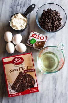 ingredients to make chocolate cake laid out on a marble counter top, including eggs and milk