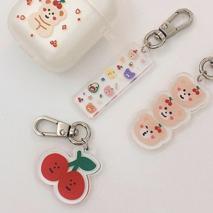 three keychains with different designs on them sitting next to an apple and strawberry