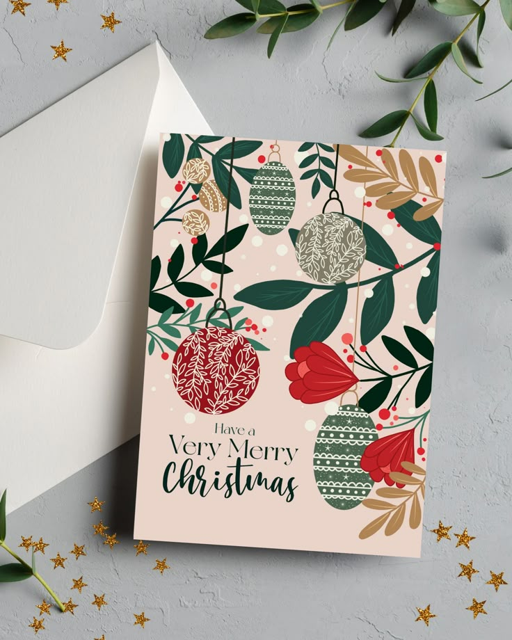 a christmas card on top of an envelope next to greenery and gold glitter stars