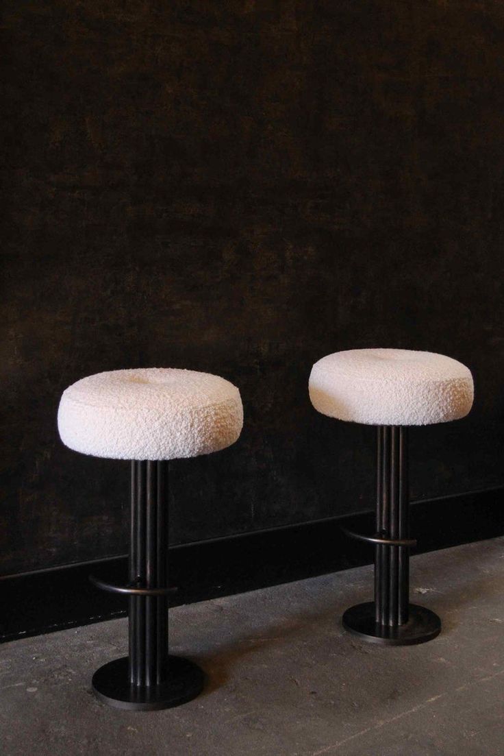 two white stools sitting next to each other in front of a black wall and floor