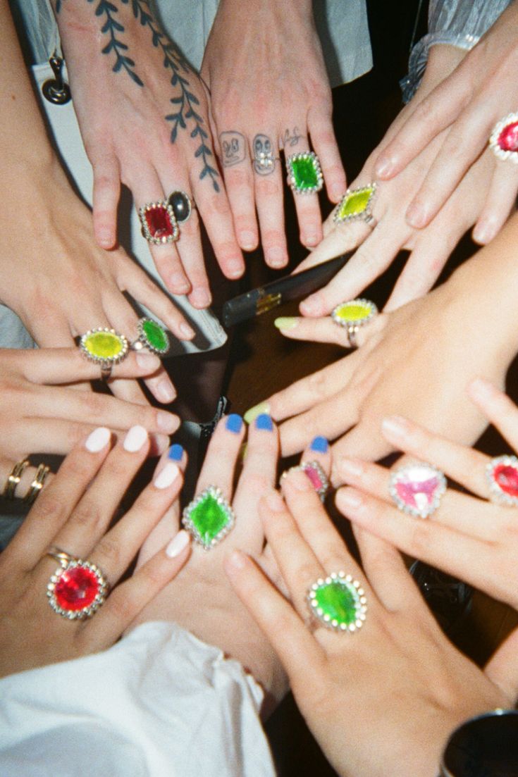 a group of people holding their hands together with different colored nails and rings on them