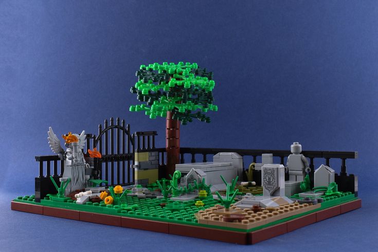 a lego model of a cemetery with trees and tombstones in the foreground, on a blue background