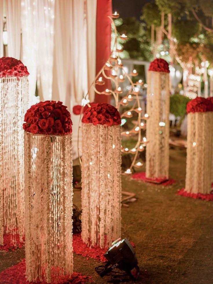 red and white flowers are placed in tall vases on the ground with lights behind them