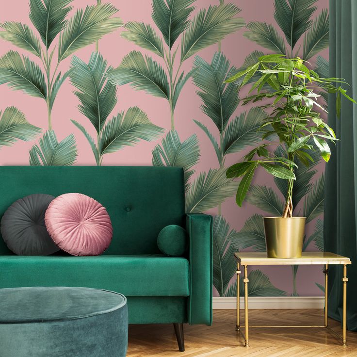 a living room with pink and green wallpaper, a velvet couch, gold side table and potted plant