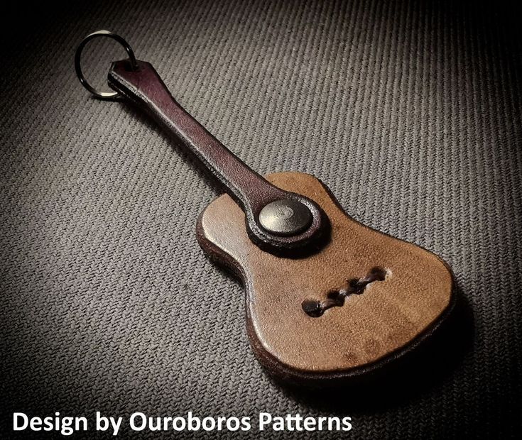 a wooden guitar keychain sitting on top of a gray surface with the words design by outdoorss patterns