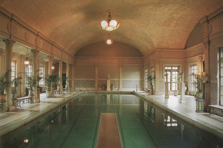 an indoor swimming pool in a large building with columns and chandeliers on either side