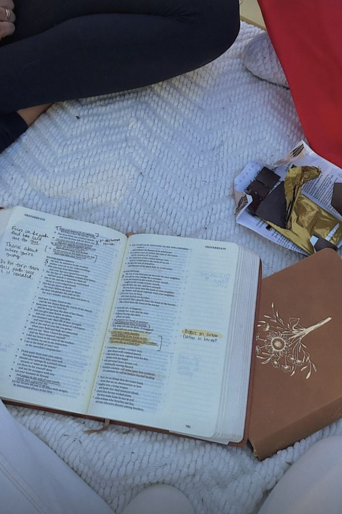 an open book sitting on top of a bed next to a box of chocolates