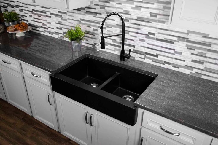 a black kitchen sink sitting under a faucet next to white cabinets and counter tops