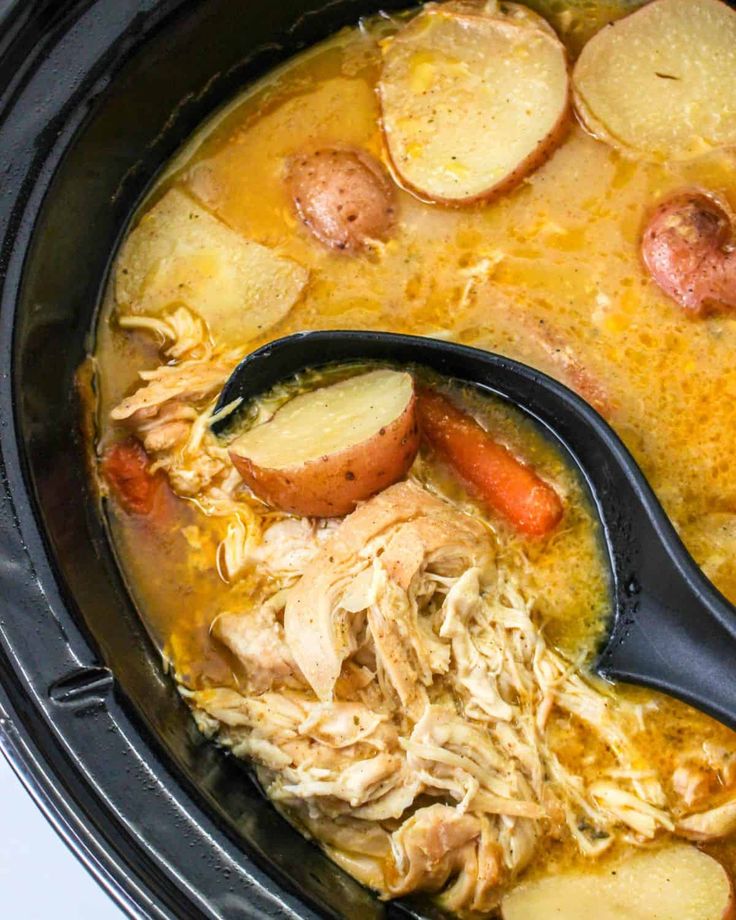 a crock pot filled with chicken, potatoes and carrots next to a spoon