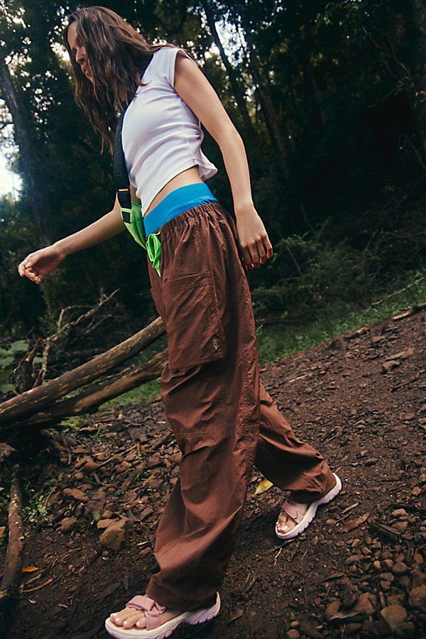 a woman in brown pants and white shirt holding a frisbee on a dirt path