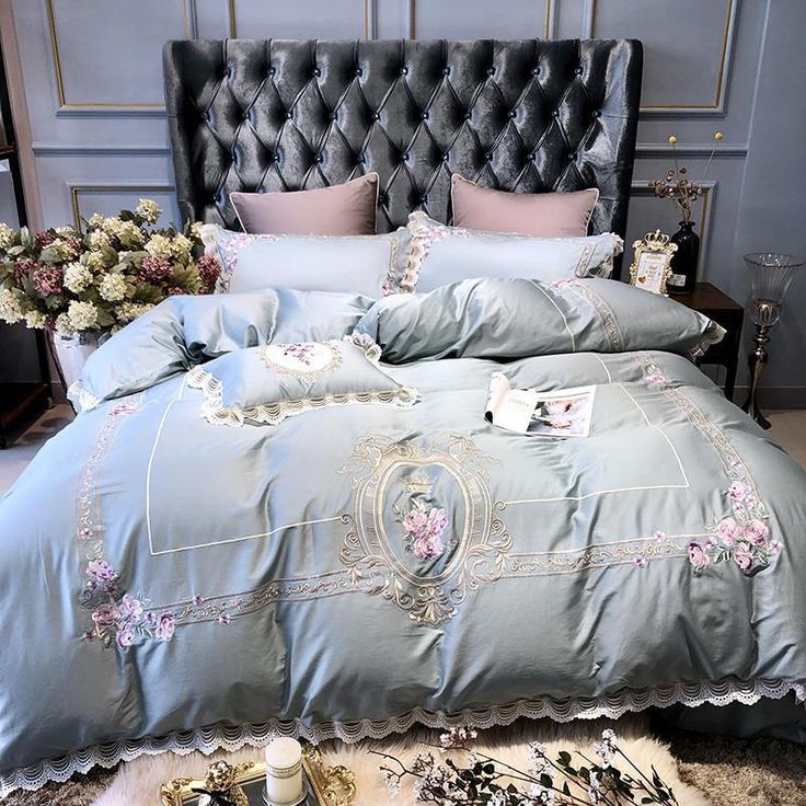 a bed with blue comforter and pillows on it in a room next to flowers