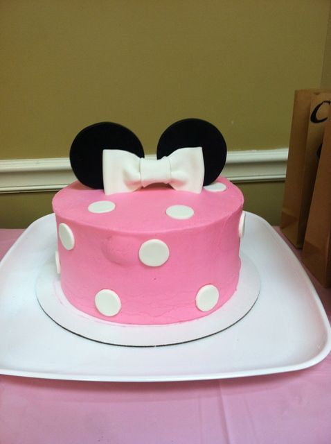 a pink and white cake with minnie mouse ears on top, sitting on a table