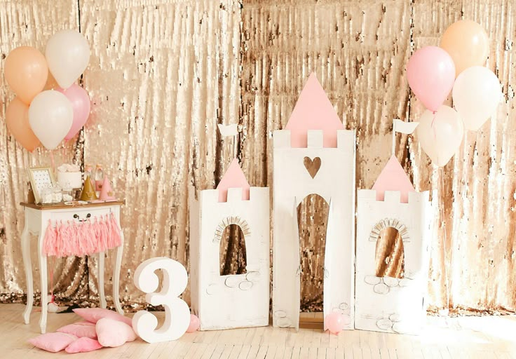 a pink and white castle with balloons on the floor in front of a gold sequin backdrop