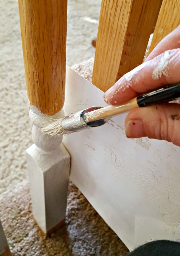 a person is holding a pencil and painting the base of a wooden railing with white paint