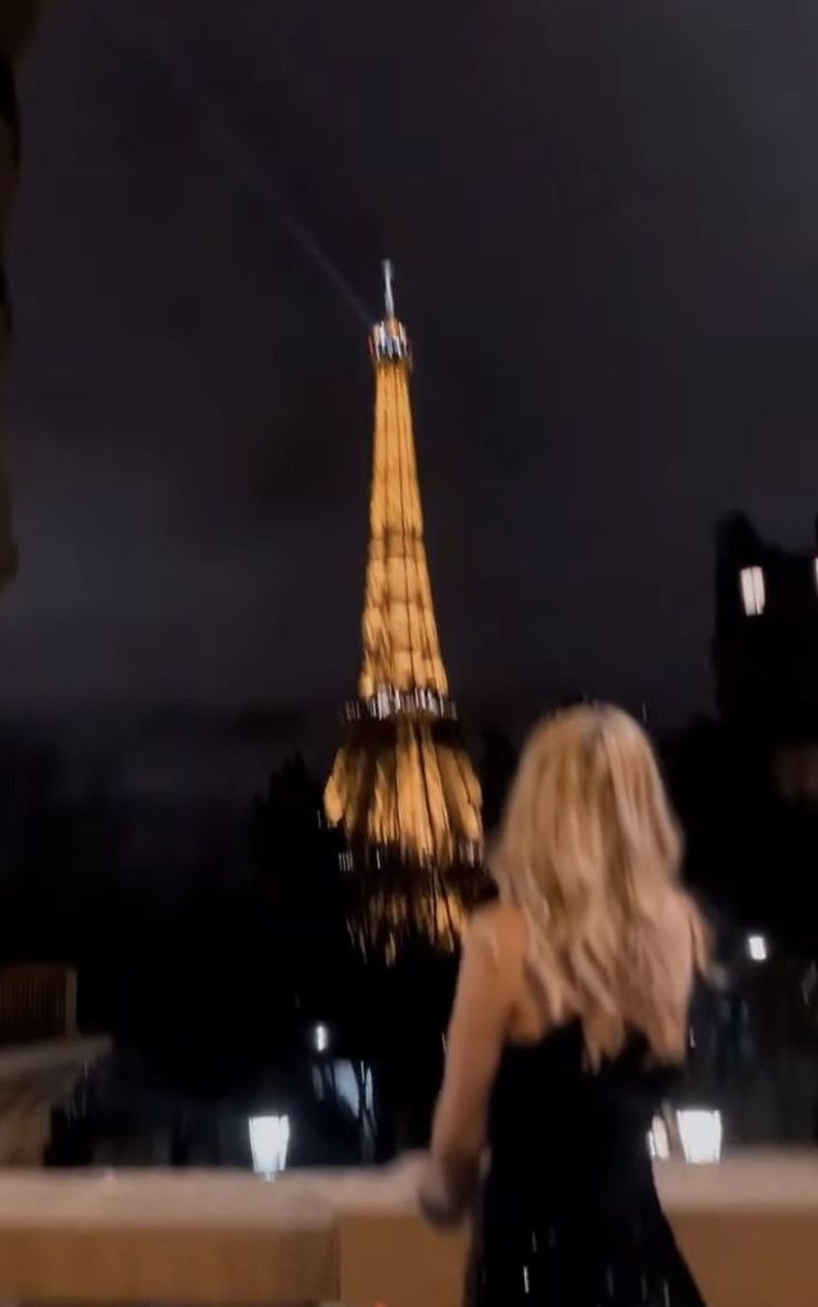 a woman in a black dress is looking at the eiffel tower