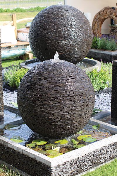 two large balls sitting on top of a fountain in the middle of a garden area