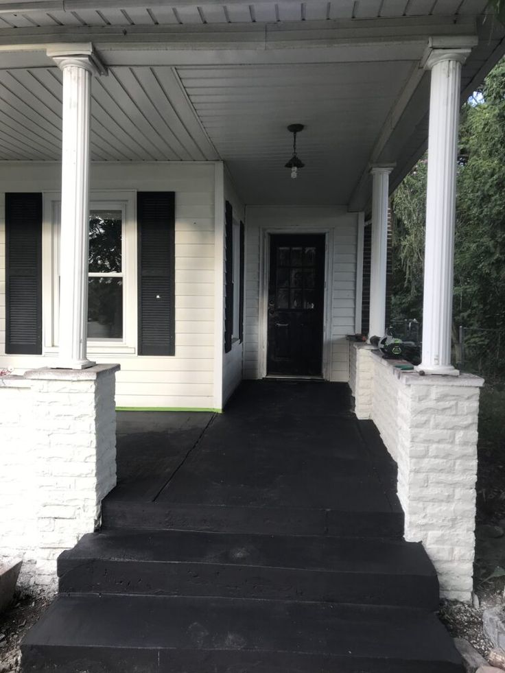 a porch with steps leading up to the front door and black shutters on both sides