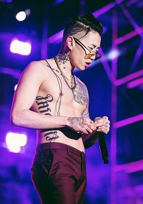 a man with tattoos on his chest holding a microphone and looking down at something in his hand