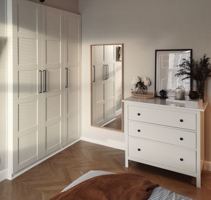 a bedroom with white furniture and wooden flooring next to a large mirror on the wall