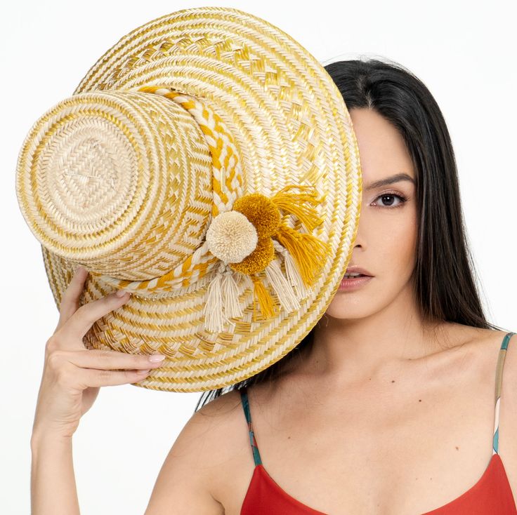 Product Description Handcrafted by Wayuu artisans. The “Caña Flecha”, which is a plant native to the region, is skillfully woven to create a wide-brimmed hat that protects from the sun and rain. Has incorporated our signature Monstera leaf and a pin style of our name tag, both gold-platted. This hat features a distinctive design that combines form and function. They are decorated with elaborate details, such as colorful ribbons and woven patterns, that reflect the rich cultural heritage of this Brimmed Panama Hat For Festival, Natural Toquilla Straw Panama Hat For Festival, Woven Toquilla Straw Panama Hat For Festival, Bohemian Brimmed Panama Hat In Palm Leaf, Handwoven Brimmed Panama Hat For Festivals, Handwoven Brimmed Sun Hat In Palm Leaf, Brimmed Handwoven Palm Leaf Sun Hat, Handwoven Toquilla Straw Boater Hat, Yellow Bohemian Bucket Hat