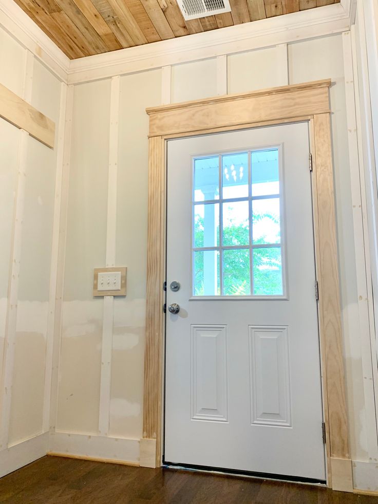 an empty room with a white door and wood paneling on the ceiling, along with a ventilator