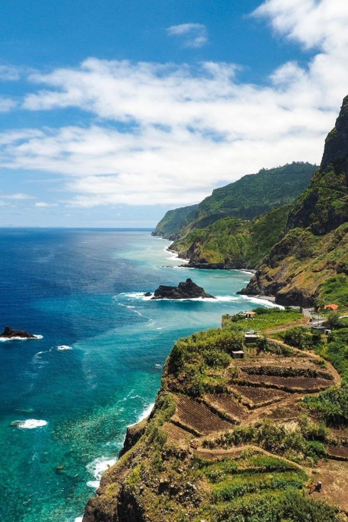 an aerial view of the ocean and coastline near a rocky cliff face with stairs leading up to it