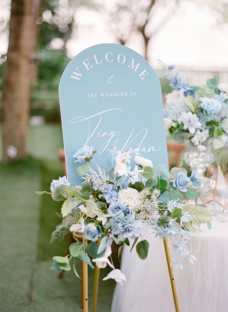 a welcome sign sitting on top of a table next to a white and blue flower arrangement