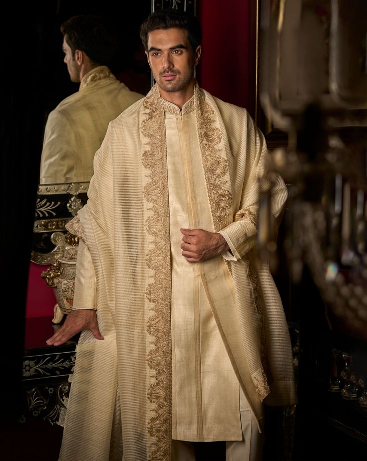 This set features stitch lines in gold thread in a stripe pattern. The collar has delicate dori embroidery. It is paired with a matching cotton silk kurta and straight pants. Complimenting stole and footwear is also available. DELIVERY TIMEPlease allow 8-12 weeks for your outfit to arrive. FABRIC DETAILSSherwani - Raw Silk, Kurta - Cotton Silk, Trouser - Cotton Silk, Dupatta - Cotton Tissue Organza Professional cleaning only. Luxury Red Men's Sherwani, Luxury Men's Salwar Kameez With Mandarin Collar, Luxury Dori Work Sets For Ceremony, Luxury Men's Bandhgala With Mandarin Collar, Luxury Designer Men's Sherwani, Luxury Men's Sherwani With Mandarin Collar, Designer Luxury Men's Sherwani, Luxury Fall Sherwani For Men, Luxury Designer Bandhgala With Mandarin Collar