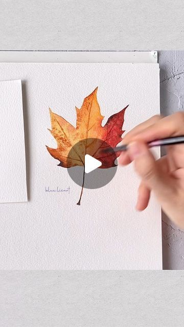 someone is painting a leaf with watercolors on paper and using a marker to draw it