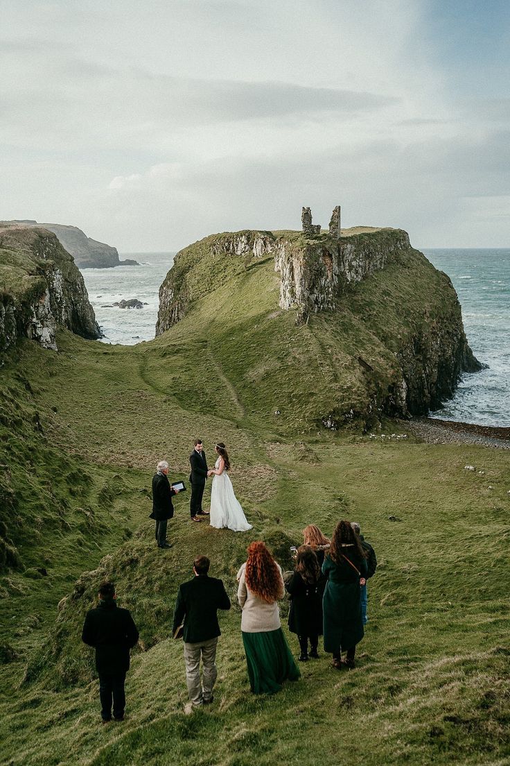 a group of people standing on top of a lush green hillside next to the ocean