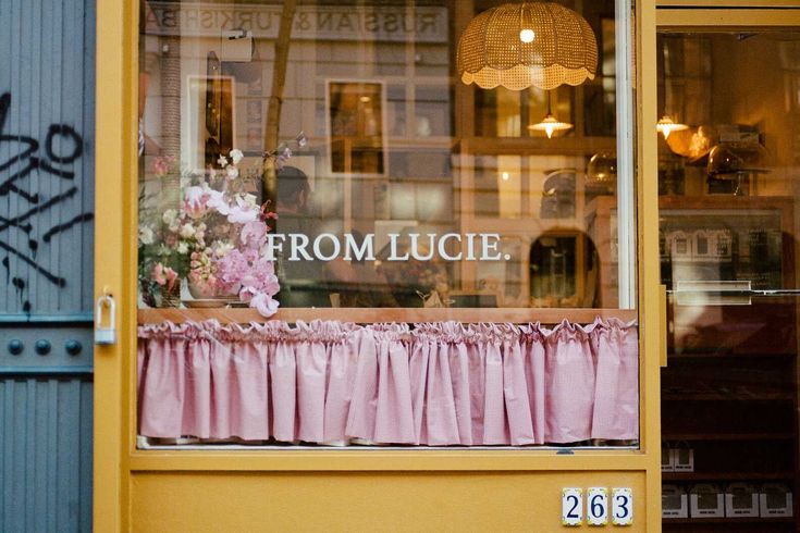 the front window of a flower shop with pink curtains