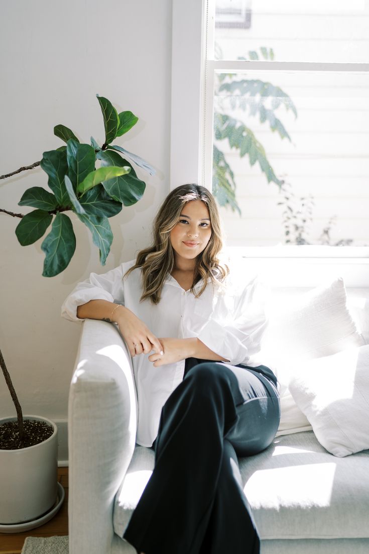 a woman sitting on top of a white couch next to a potted plant