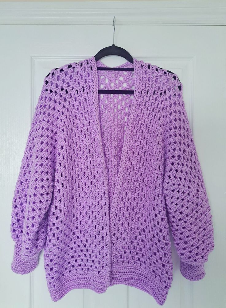 a purple crocheted cardigan hanging on a white door with a black hanger