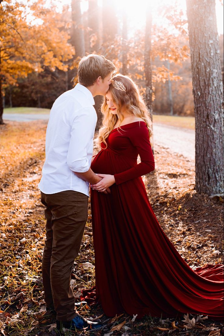 a pregnant woman in a red dress standing next to a man