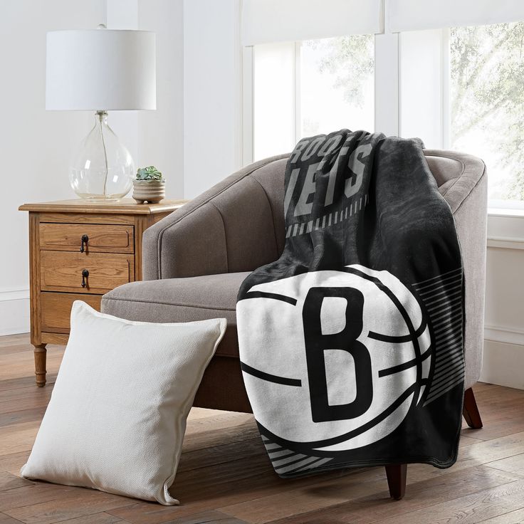 a basketball blanket sitting on top of a couch next to two pillows and a lamp