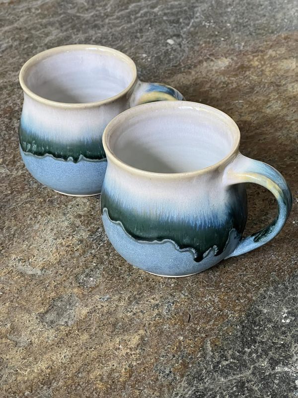 two coffee mugs sitting on top of a granite countertop next to each other