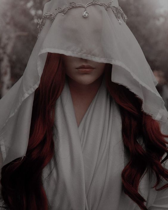 a woman with long red hair wearing a veil over her head and covering her face