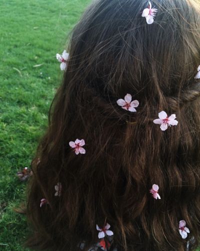 the back of a woman's head with pink flowers in her hair on green grass