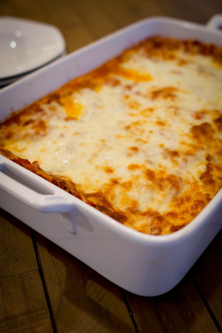 a white casserole dish with cheese on it sitting on top of a wooden table