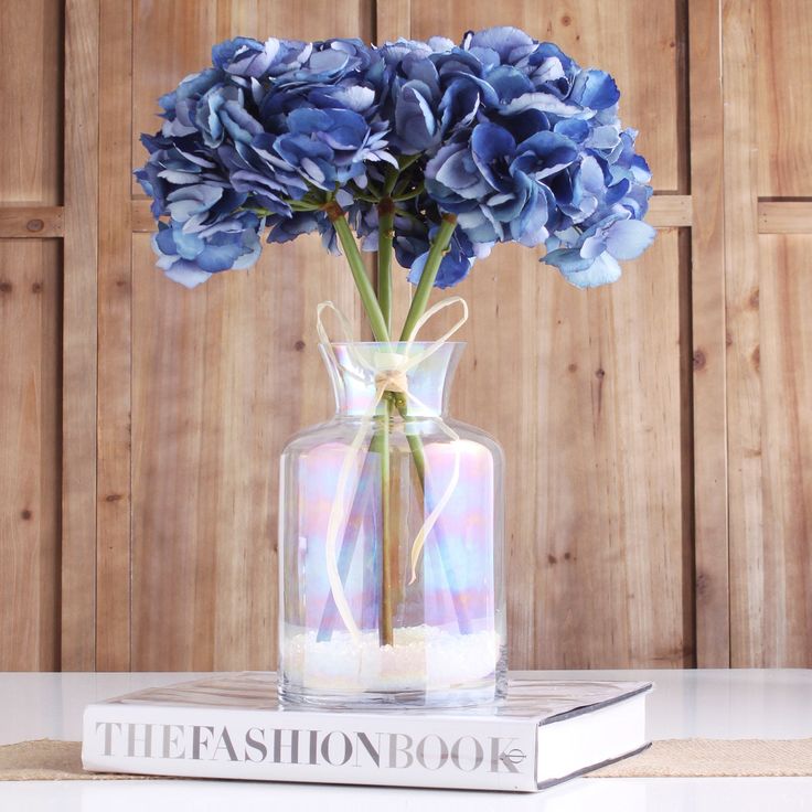 a blue flower in a glass vase on top of a book