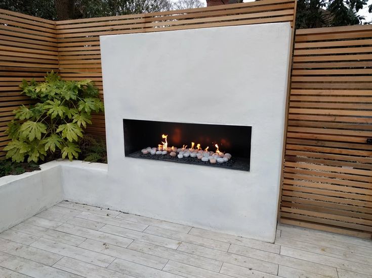 a fire place in the middle of a patio with candles on it and a wooden fence behind it