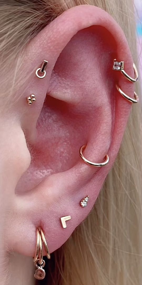 an ear with three different types of piercings on it's sides and one is gold